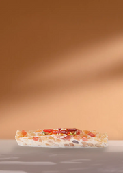 Une délicieuse barre de nougat présentant une gamme de noix et de fruits secs colorés, délicieusement emballés et portant fièrement le nom de la marque « Turrón de Jijona », présentés sur un simple fond beige. Parfaitement conçu pour compléter vos moments café ! | Flaronis.lu