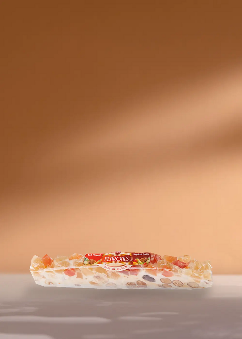 Une délicieuse barre de nougat présentant une gamme de noix et de fruits secs colorés, délicieusement emballés et portant fièrement le nom de la marque « Turrón de Jijona », présentés sur un simple fond beige. Parfaitement conçu pour compléter vos moments café ! | Flaronis.lu