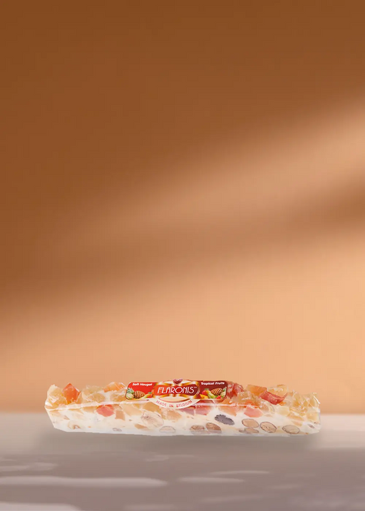 Une délicieuse barre de nougat présentant une gamme de noix et de fruits secs colorés, délicieusement emballés et portant fièrement le nom de la marque « Turrón de Jijona », présentés sur un simple fond beige. Parfaitement conçu pour compléter vos moments café ! | Flaronis.lu