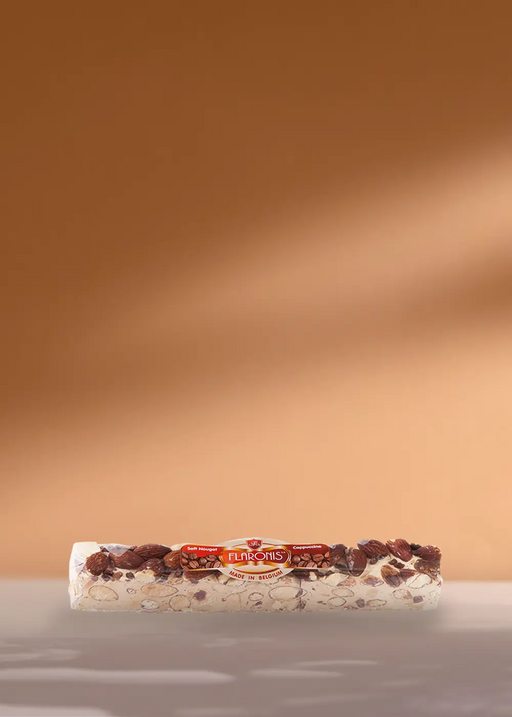 Une délicieuse barre de 100 g de Nougat Tendre Cappuccino Flaronis, remplie de noix croquantes, repose sur une surface chaude de couleur cappuccino, parfaite pour les amateurs de café à la recherche d'une friandise sucrée ! | Flaronis.lu