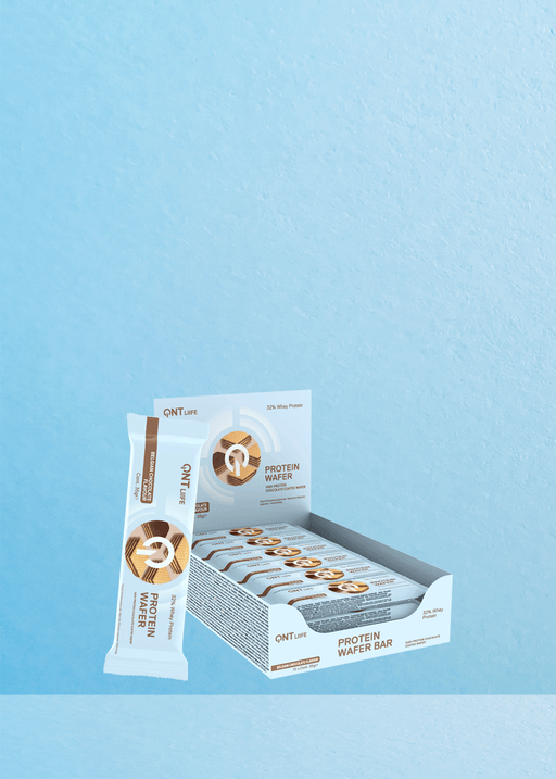 Imaginez une boîte de gaufrettes protéinées QNT 32 % de chocolat joliment disposée sur un fond bleu, avec une délicieuse barre qui vous invite à sortir de son emballage. Parfait pour les amateurs de café, cette friandise se marie à merveille avec votre boisson préférée. L'emballage présente des illustrations alléchantes de chocolat et de gaufrettes croustillantes tout en soulignant son impressionnante teneur en protéines de 32 % pour vous garder en forme tout au long de la journée. | Flaronis.lu