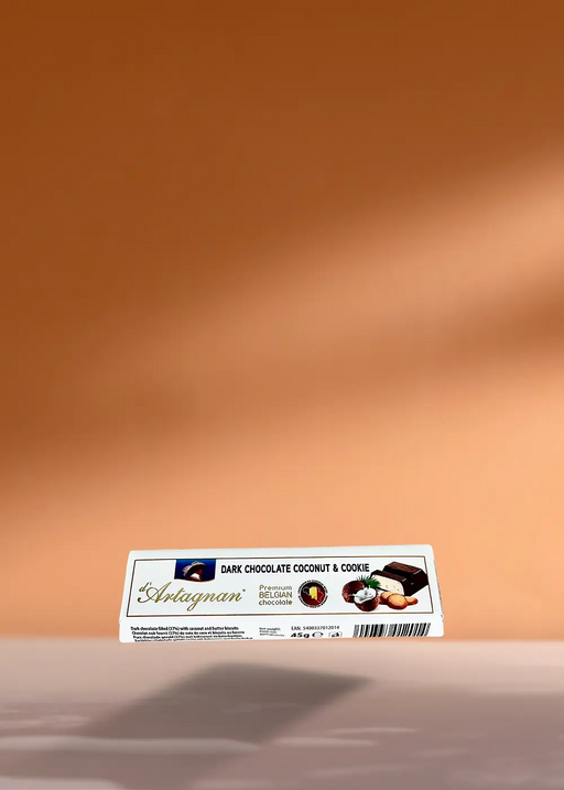 Un élégant paquet rectangulaire de chocolat noir Bâton d'Artagnan à la noix de coco et au biscuit, pesant 45 g, repose de manière invitante sur un fond de pêche chaleureux, son ombre murmurant des histoires de gourmandise, parfait pour les amateurs de café à la recherche d'un accord délicieux. | Flaronis.lu