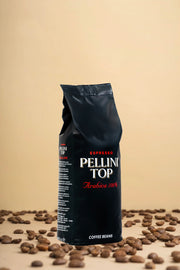 Découvrez l'élégance du café avec un élégant présentoir présentant un sac noir de 500 g de grains Pellini Top 100 % Arabica. Imaginez ces grains de café haut de gamme, disposés avec art sur une surface beige chaleureuse, vous invitant à savourer leur arôme riche et leur saveur exquise. Parfait pour les vrais amateurs de café !. | Flaronis.lu