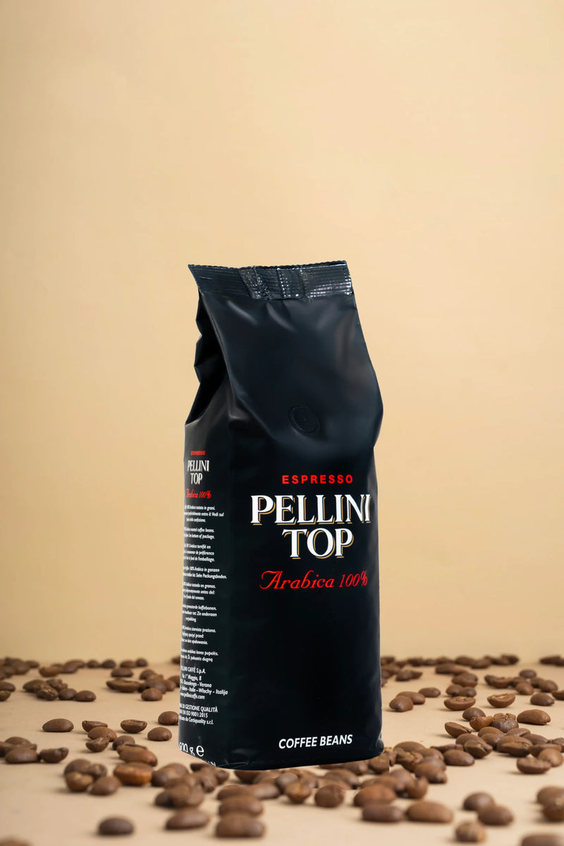 Découvrez l'élégance du café avec un élégant présentoir présentant un sac noir de 500 g de grains Pellini Top 100 % Arabica. Imaginez ces grains de café haut de gamme, disposés avec art sur une surface beige chaleureuse, vous invitant à savourer leur arôme riche et leur saveur exquise. Parfait pour les vrais amateurs de café !. | Flaronis.lu